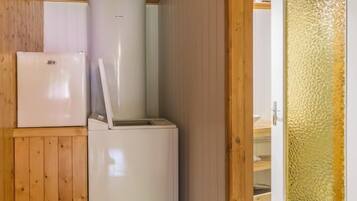 Une cuisine de taille réduite, équipée d’un réfrigérateur et d’un évier, avec des murs en bois et une porte dotée d’un panneau en verre texturé.
