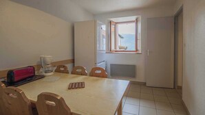 Ein kleiner, gemütlicher Raum mit einem Holztisch, Stühlen, einer Kaffeemaschine und einem Fenster mit Blick ins Freie.