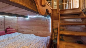 Quarto de cabana de madeira com cama, escada e janela.
