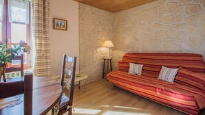 Une pièce chaleureuse avec un mur en pierre, un plafond en bois, un canapé à rayures rouges, une table à manger en bois avec des chaises et une petite table avec une lampe.