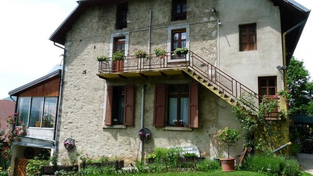 Une maison en pierre à deux étages, dotée d’un balcon, de plantes en pot et d’un petit jardin.