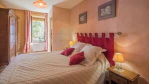 Une chambre à coucher avec un lit, deux lampes de chevet, une fenêtre avec des rideaux et deux tableaux encadrés accrochés au mur.