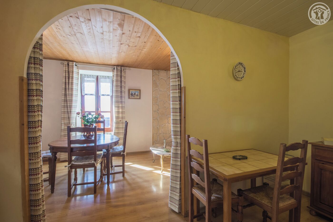 Un coin repas avec une table et des chaises en bois, un mur en pierre et une horloge au mur.