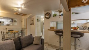 A modern living room with a grey sofa, a dining area with a glass table, and a kitchen with a bar area. - LA TARINE N°8 - PALLUD (PALLUD)