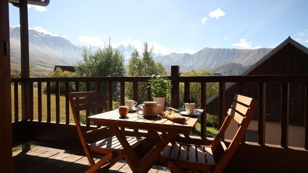 A wooden deck with a table set for breakfast, overlooking a mountainous landscape.