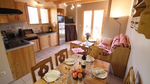 A cozy kitchen with wooden cabinets, a dining table set for two, and a sofa in the background.