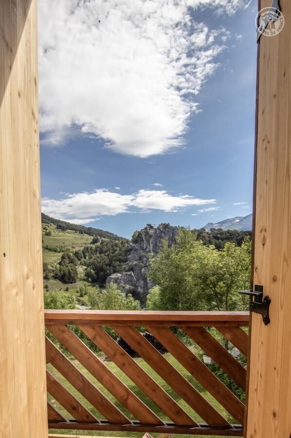 A wooden balcony with a view of a mountainous landscape and a clear sky.
