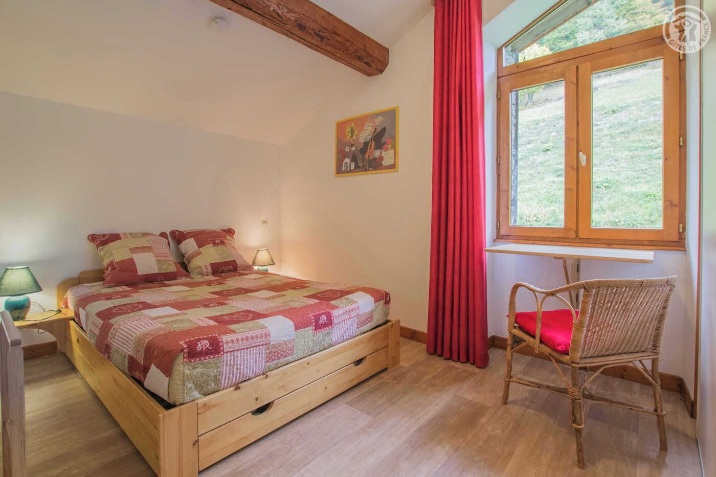 Une chambre à coucher avec un lit en bois, une chaise, une fenêtre avec des rideaux et un tableau accroché au mur.