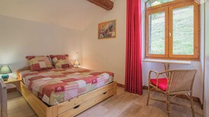 Une chambre à coucher avec un lit en bois, une chaise, une fenêtre avec des rideaux et un tableau accroché au mur.