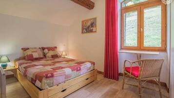 Une chambre à coucher avec un lit en bois, une chaise, une fenêtre avec des rideaux et un tableau accroché au mur.