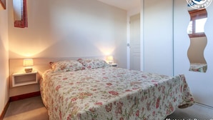 A bedroom with a floral bedspread, bedside lamps, a wooden nightstand, and a wardrobe with a mirror. - BELLE VUE - VEREL PRAGONDRAN (VEREL PRAGONDRAN)