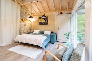 A bedroom with a bed, a window, a stone wall, and a wooden ceiling. - LA BERGERIE - MEYRIEUX TROUET (MEYRIEUX TROUET)