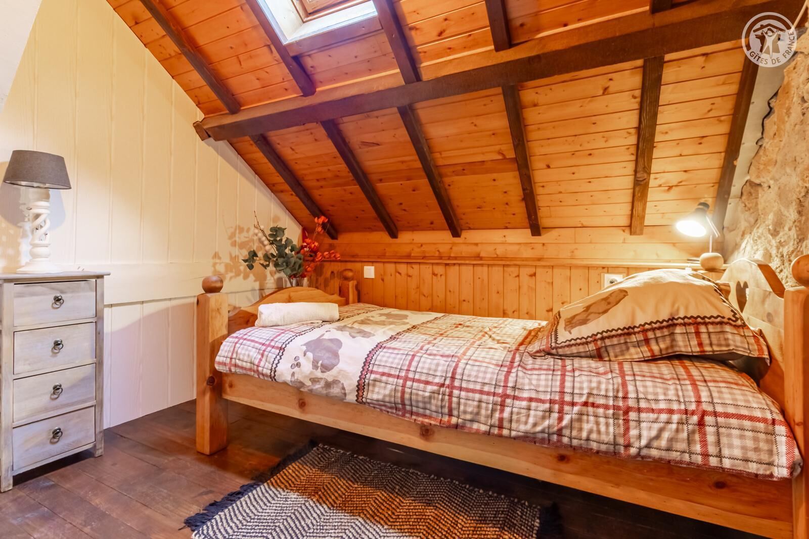 A cozy attic bedroom with a wooden bed, a dresser, and a skylight.
