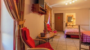 A cozy room with a bed, a chair, a small table, and a mirror.