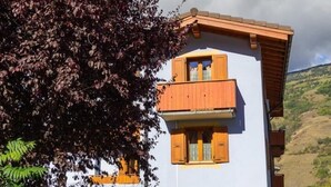 A two-story building with wooden balconies and a pink facade, surrounded by greenery and a clear sky.