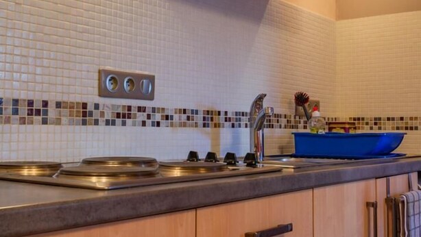 A kitchen with wooden cabinets, a tiled backsplash, and a blue dish rack.