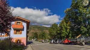 A street view with a two-story building, parked cars, and a mountain in the background.