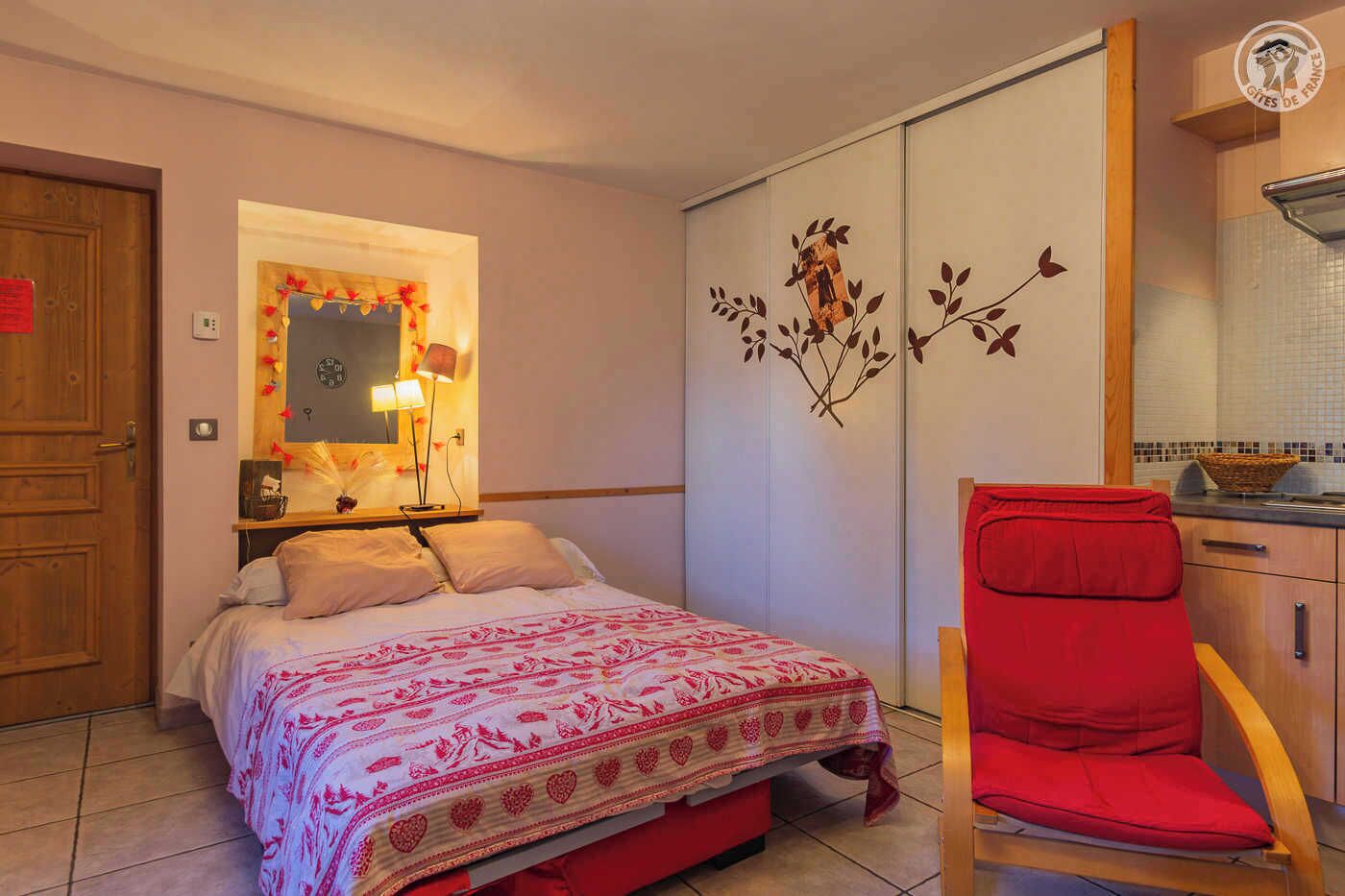 Una camera da letto con un letto, una sedia rossa, un armadio e uno specchio.