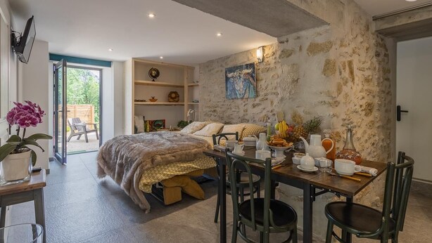 A cozy room with a bed, a dining table set with dishes, and a stone wall. - L'ETERNELLE - TRAIZE (TRAIZE)