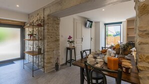 A dining area with a stone wall, a metal shelf with plants, a wooden table with various items, and a TV mounted on the wall. - L'ETERNELLE - TRAIZE (TRAIZE)