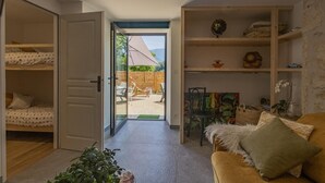 A cozy room with a sofa, a coffee table, and a bookshelf. There is a door leading to an outdoor area with a table and chairs. - L'ETERNELLE - TRAIZE (TRAIZE)