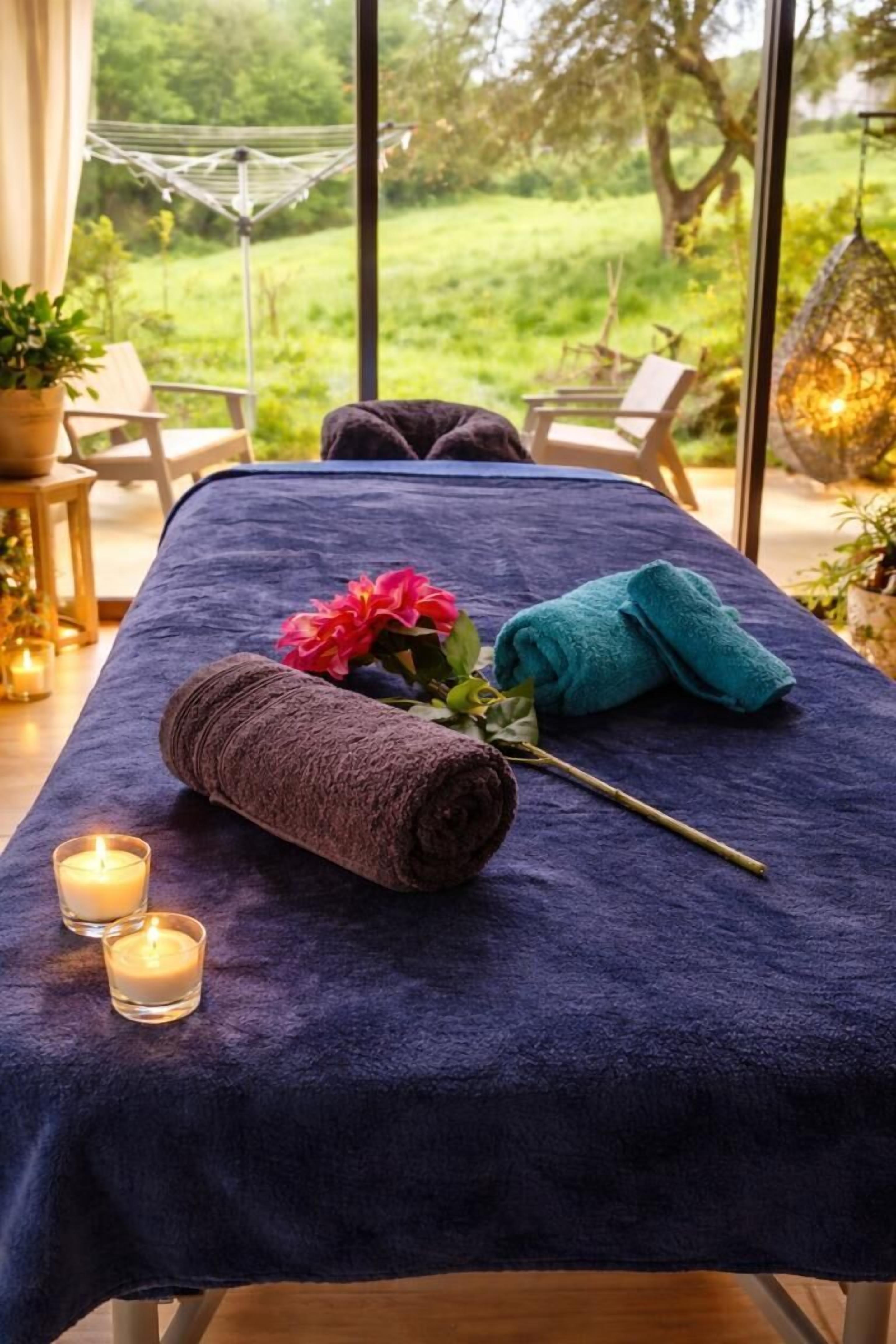 Ein Massagetisch mit Handtüchern, einer Blume und Kerzen.