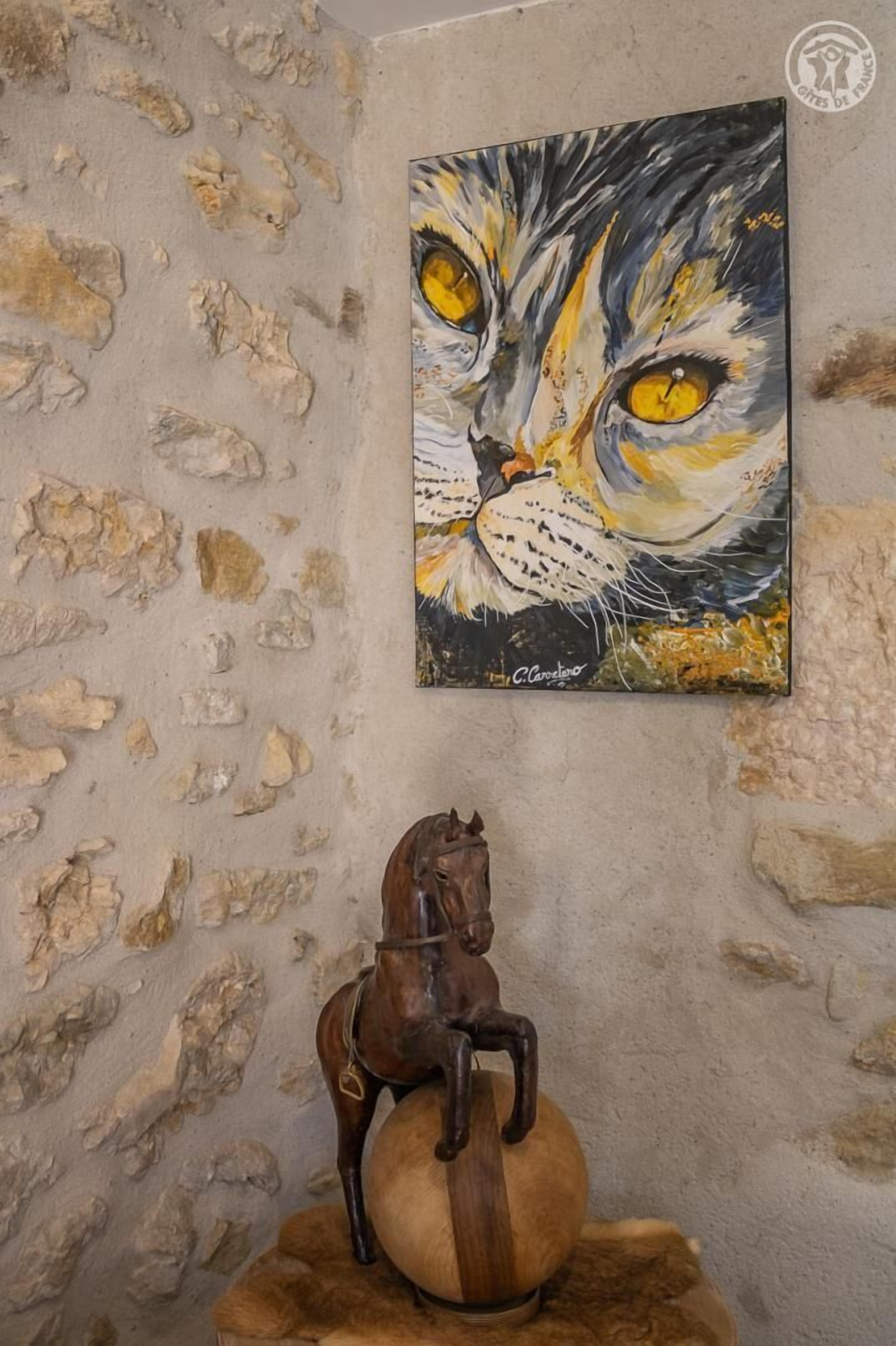 Mur de pedra amb un quadre d'un gat i una escultura de cavall de fusta.