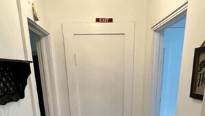 Un couloir étroit doté d’un plancher en bois, d’un paillasson noir et d’une porte blanche sur laquelle est apposée une pancarte indiquant « SORTIE ».