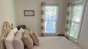 Une chambre à coucher avec un lit, une table de chevet, une petite plante en pot et une fenêtre avec des stores.