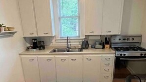 Une cuisine avec des armoires blanches, un plan de travail noir, une cuisinière et une fenêtre.