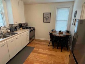 Une cuisine de taille réduite, avec des meubles blancs, une cuisinière et un coin repas comprenant une table et des chaises.