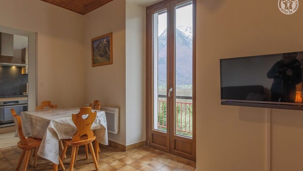Ein Essbereich mit Tisch und Stühlen, eine Küche, ein großes Fenster mit Blick und ein wandmontierter Fernseher.