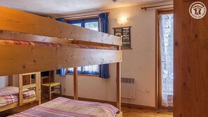 Une chambre de dortoir avec des lits superposés, une petite table et une fenêtre avec des rideaux.