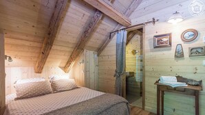 A cozy wooden room with a bed, a small table, and a door leading to another room.