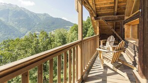 A wooden deck with a view of mountains, wooden chairs, and a table.
