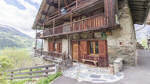 A traditional chalet with a stone facade, wooden balconies, and a stone staircase leading to the entrance.