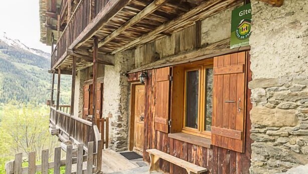 A rustic building with a wooden balcony and stone steps. A sign reads "Le Gentiane."