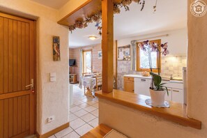 A wooden-framed window with a potted plant, a kitchen area with a sink and cabinets, and a dining area with a table and chairs. - LE VIROLET - BEAUFORT ARECHES (BEAUFORT ARECHES)