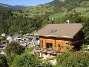 A wooden chalet with a balcony, surrounded by lush greenery and a mountainous backdrop. - LE VIROLET - BEAUFORT ARECHES (BEAUFORT ARECHES)