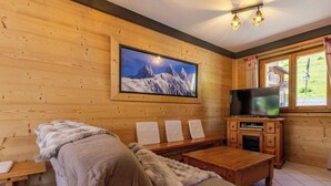 A cozy room with a wooden interior, a large framed picture of a mountain, a television, and a sofa with a fur throw. - CHALET L'ALBARON - SAINT SORLIN D'ARVES (SAINT SORLIN D'ARVES)
