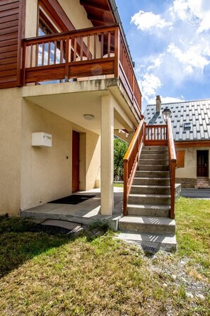 A building with a wooden balcony, a concrete staircase, and a door leading to the entrance.