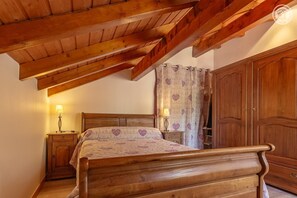 A bedroom with a wooden bed, a nightstand, a wardrobe, and a ceiling with exposed beams.