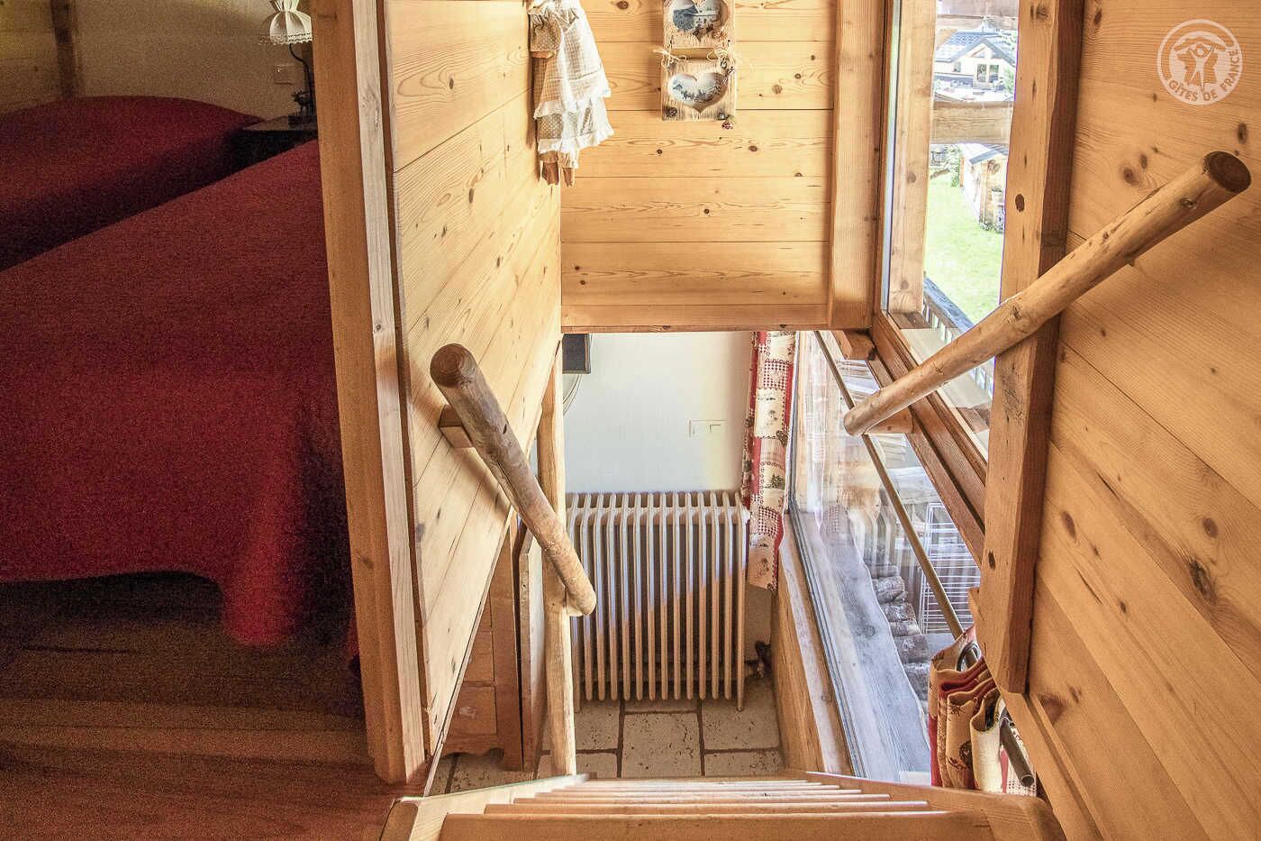Een houten interieur met een rode bed, een houten trap en uitzicht op het exterieur.