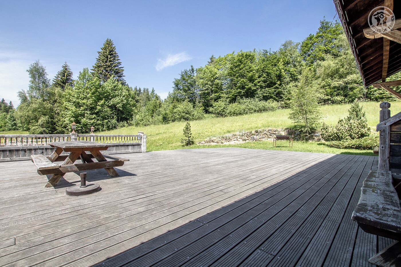 Eine Holzterrasse mit Picknicktisch, umgeben von einem Geländer und Blick auf einen bewaldeten Hügel.