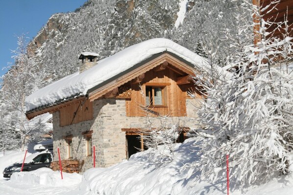 A stone cabin with a wooden roof and chimney, surrounded by snow-covered trees.
