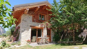 A rustic wooden chalet with a stone facade, a wooden porch, and a garden with flowering plants.