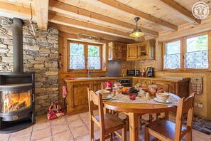 A cozy cabin-style kitchen with a wood-burning stove, stone wall, wooden cabinets, and a dining table set for breakfast.