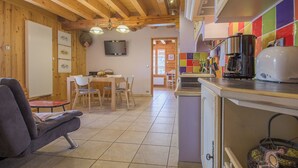 A cozy room with a sofa, a dining table with chairs, a kitchen area with a coffee machine, and a TV mounted on the wall. - LA GRIVE - CLERY - Gîte (CLERY)