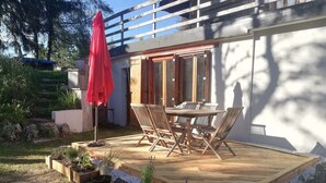 Une terrasse en bois avec une table et des chaises, entourée d’un jardin planté et agrémentée d’un parasol rouge.