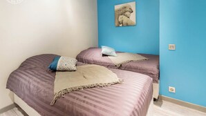A bedroom with two beds, each with patterned bedding and pillows. A painting of a polar bear is on the blue wall.